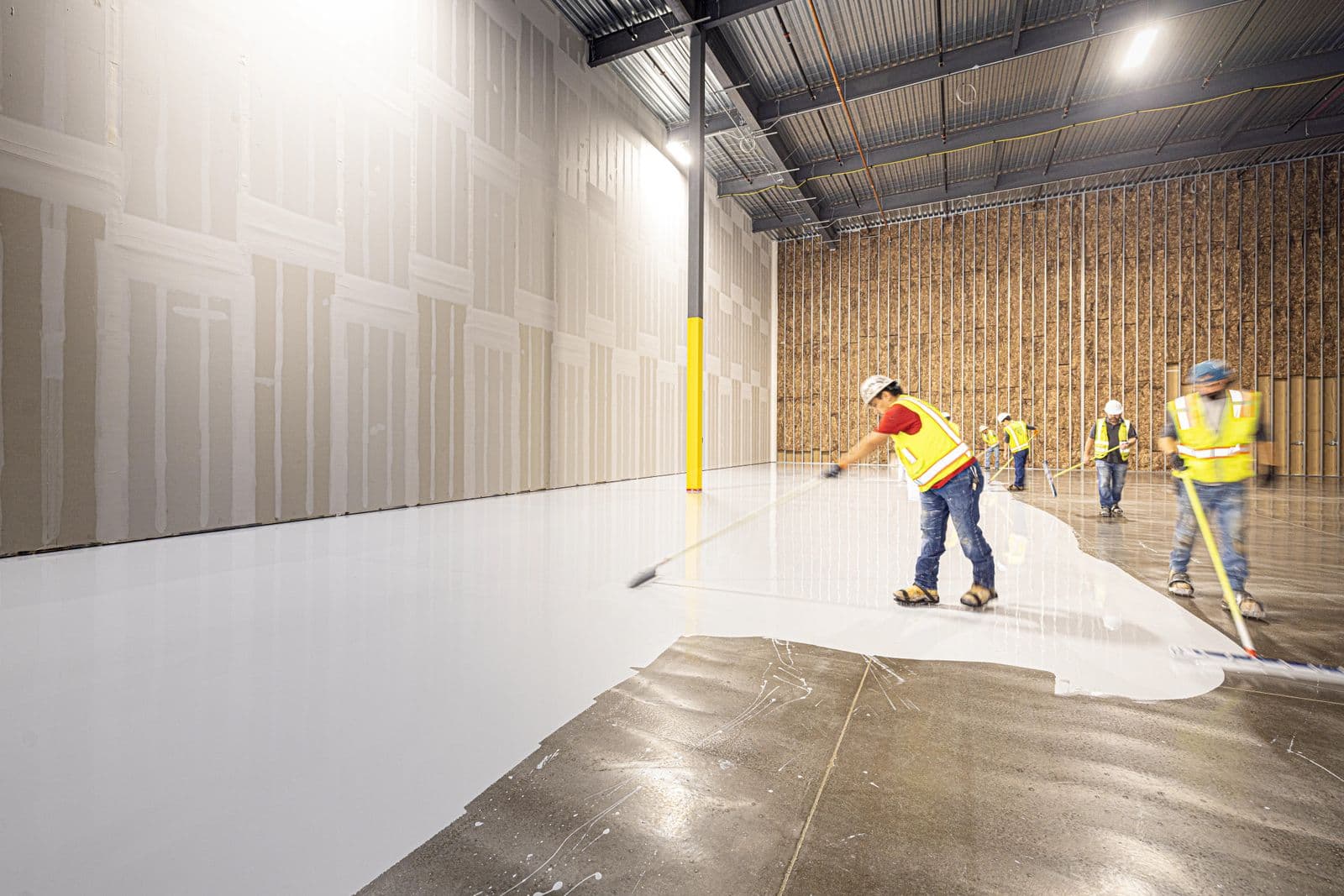 Certified installers in hard hats and safety vests squeegeeing a self-leveling epoxy coating across a commercial floor